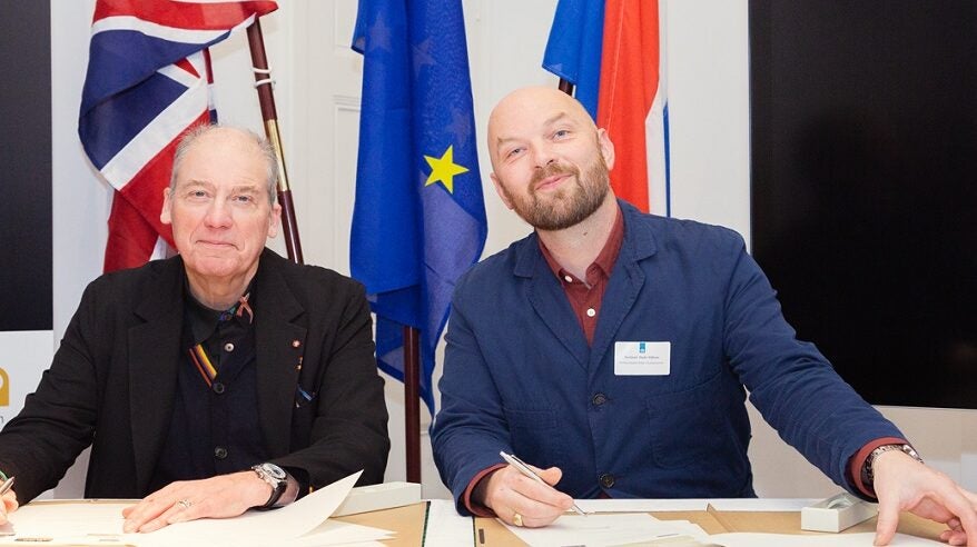 Adrian Wootton and Roeland Oude Nijhuis sit at a desk to sign a memorandum of understanding between the UK and Dutch screen industries