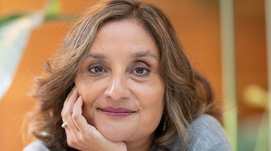 Headshot of TV executive Angela Jain, with her chin on her hand against an orange background
