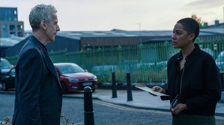 Scene from drama Criminal Record, with actors Peter Capaldi and Jumbo Cush standing face to face on a London street with cars and an industrial building in the background