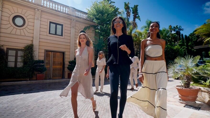 Very glamorous ladies walk down a street with blue sky and palm trees behind