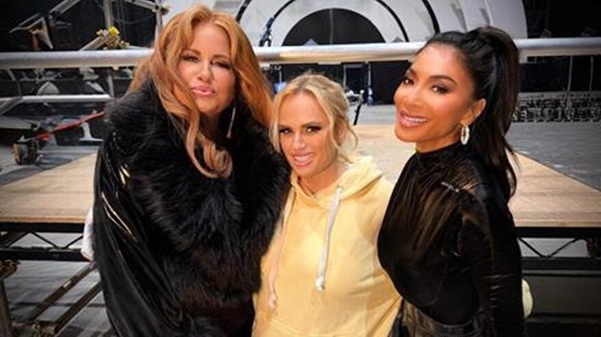 Three glamorous ladies stand in a row, smiling to camera