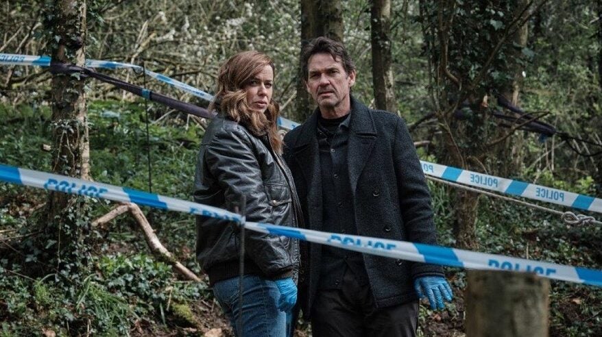 A woman and a man stand in a wooded area, within a police tape cordon, from drama The Crow Girl