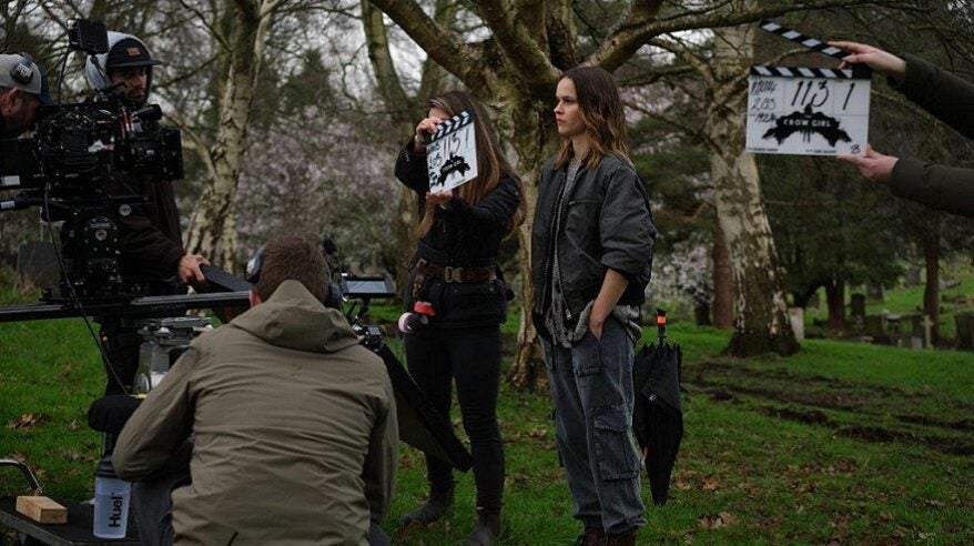 A camera operator films a woman standing in a cemetery , with a person holding a clapperboard behind, from Paramount+ drama The Crow Girl